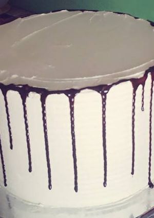 A picture of Rainbow cake decorated with butter cream and chocolate drips.