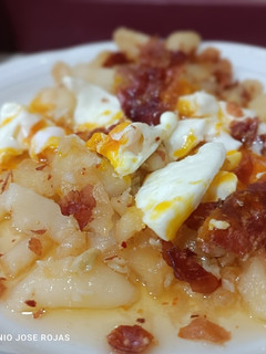 Una foto de Huevos rotos en patatas confitadas picantes y jamón seco