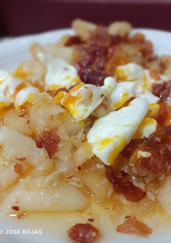Una foto de Huevos rotos en patatas confitadas picantes y jamón seco