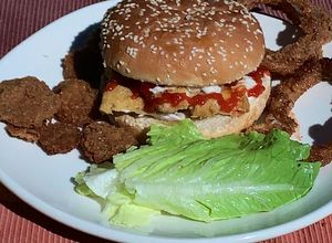 Una foto de Hamburguesa de pescado estilo Sitka Alaska con guarnición de aros de cebolla y pepinillos fritos