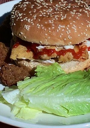 Una foto de Hamburguesa de pescado estilo Sitka Alaska con guarnición de aros de cebolla y pepinillos fritos