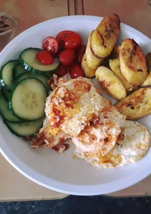 A picture of Fried plantain with fried egg served with cucumber and fresh tomatoes.