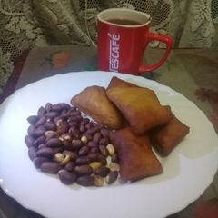 A picture of Roasted nuts, cardamom mandazi n a cup of hot black Nescafe.