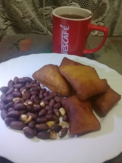 A picture of Roasted nuts, cardamom mandazi n a cup of hot black Nescafe.