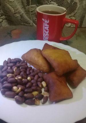 A picture of Roasted nuts, cardamom mandazi n a cup of hot black Nescafe.