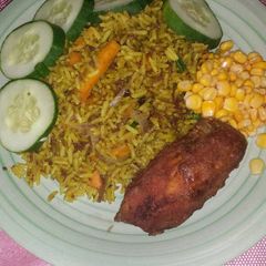 A picture of Fried rice garnished with sweet corn, cucumber and fried chicken.