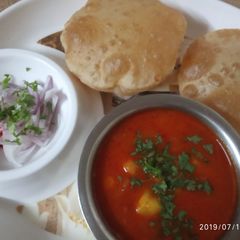 A picture of Aloo-tamatar ki khatti sabji with puri and onion salad.