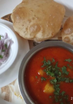 A picture of Aloo-tamatar ki khatti sabji with puri and onion salad.