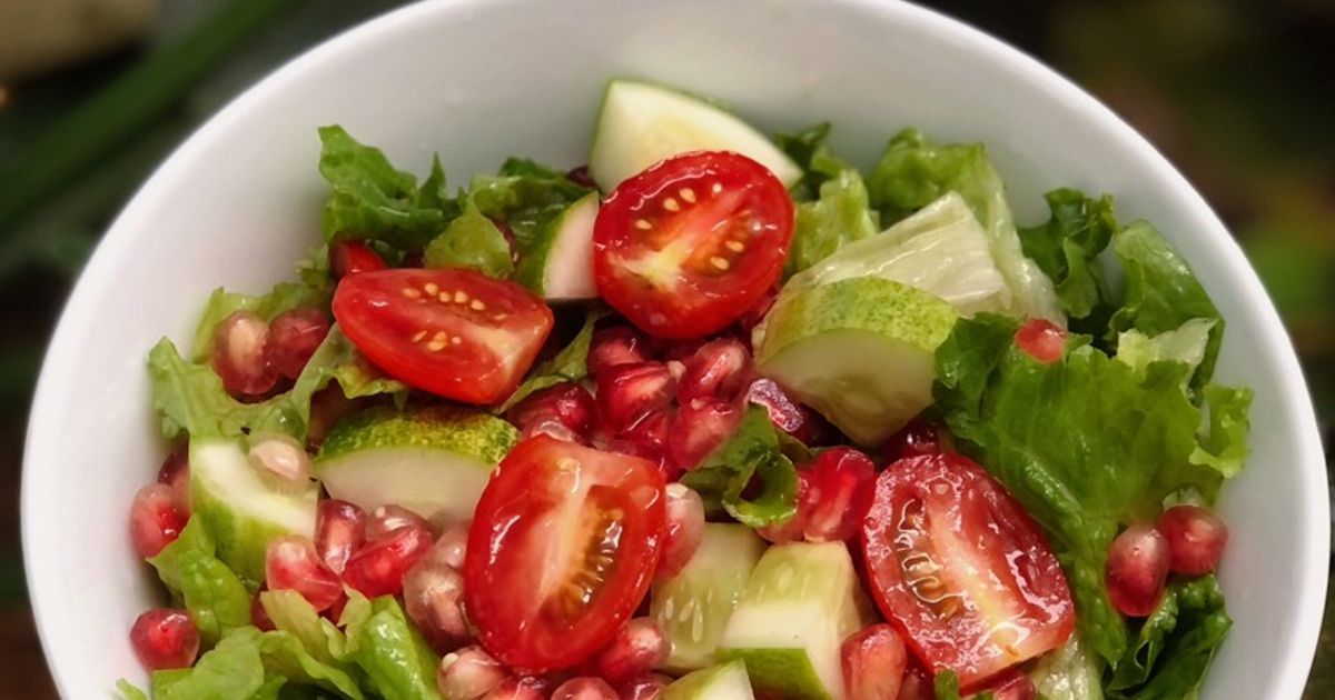 Bát salad gồm rau xà lách, cà chua bi, dưa leo và hạt lựu, tạo nên món ăn tươi ngon và màu sắc hấp dẫn.