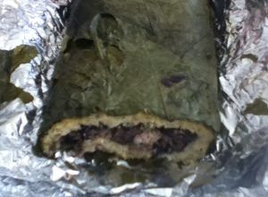 Una foto de Tamal enrollado de frijol negro, masa y hoja santa