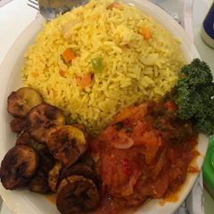 A picture of Fried rice n plantain with chicken sauce garnished with kale leaf.