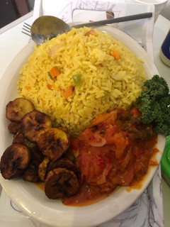 A picture of Fried rice n plantain with chicken sauce garnished with kale leaf.