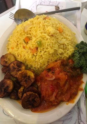 A picture of Fried rice n plantain with chicken sauce garnished with kale leaf.