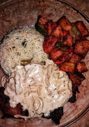 A picture of Chicken steak with mushroom sauce with fried rice and fried vegetables.