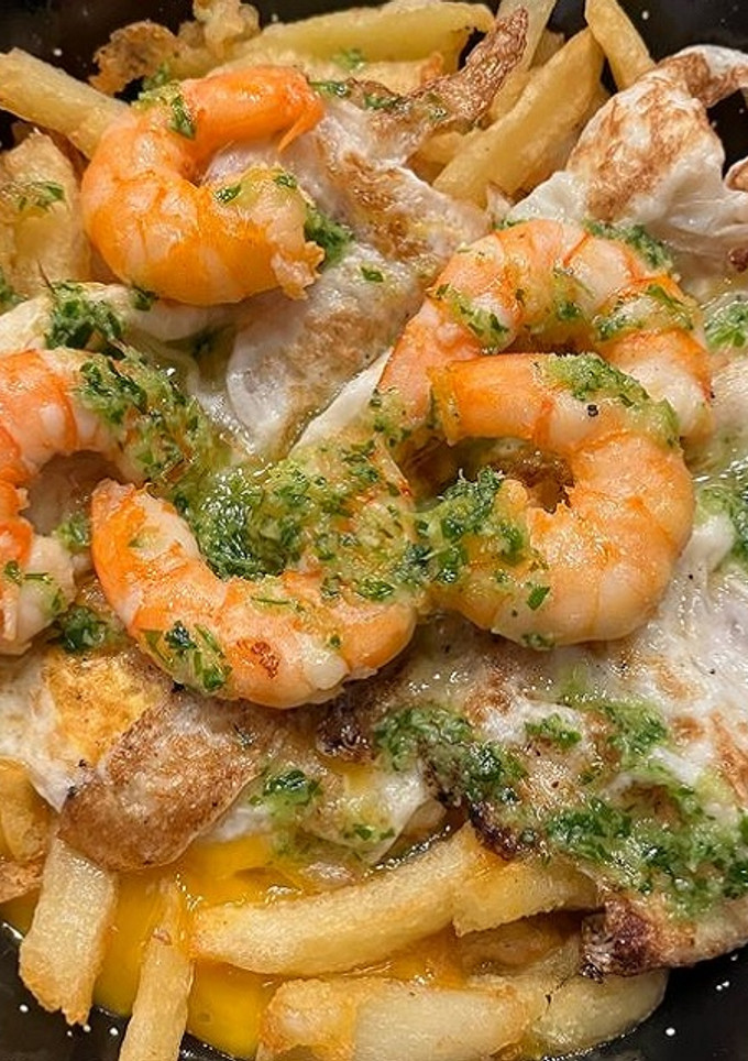 Una foto de Patatas fritas con huevos rotos y langostinos al ajillo