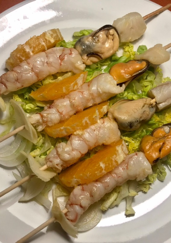 Una foto de Pincho de ceviche de pescado, mejillones y gambones, sobre cama de verduras crudas y frutas