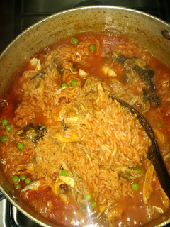 A picture of Jollof rice with green peas and smoked fish.