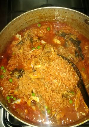 A picture of Jollof rice with green peas and smoked fish.