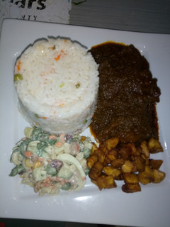 A picture of Green pepper sauce with white rice and plantain + salad.