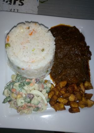 A picture of Green pepper sauce with white rice and plantain + salad.