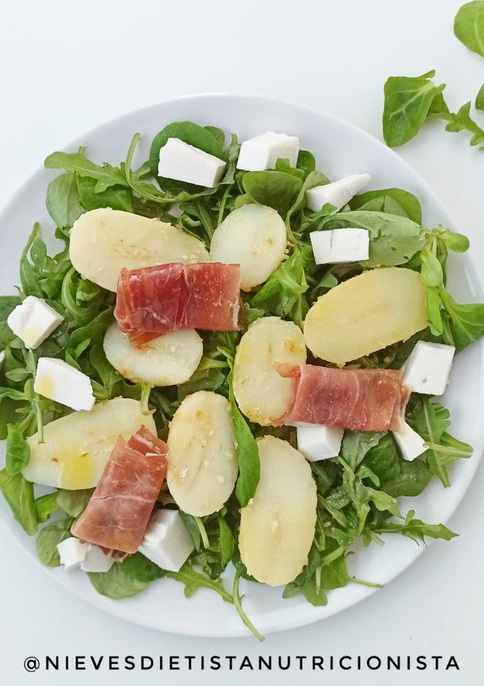Una foto de Ensalada de canónigos, patata asada, queso fresco de cabra y jamón serrano