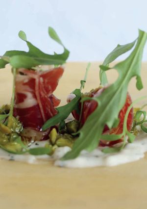 Una foto de Jamón serrano, crema de queso manchego, rúcula y pistacho