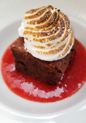Una foto de Brownie de avellanas con salsa de fresas y merengue