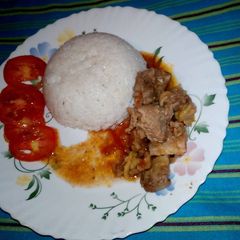A picture of Boiled rice /beef stew garnished with tomatoes.