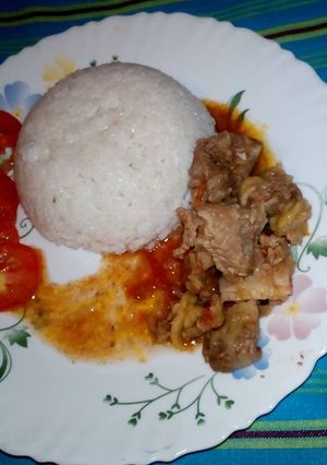 A picture of Boiled rice /beef stew garnished with tomatoes.