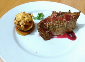 Una foto de Carre de cerdo macerado en finas hierbas con salsa de cítricos y frutos rojos, con torre de vegetales gratinado