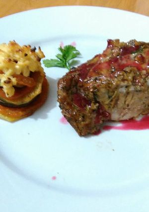 Una foto de Carre de cerdo macerado en finas hierbas con salsa de cítricos y frutos rojos, con torre de vegetales gratinado