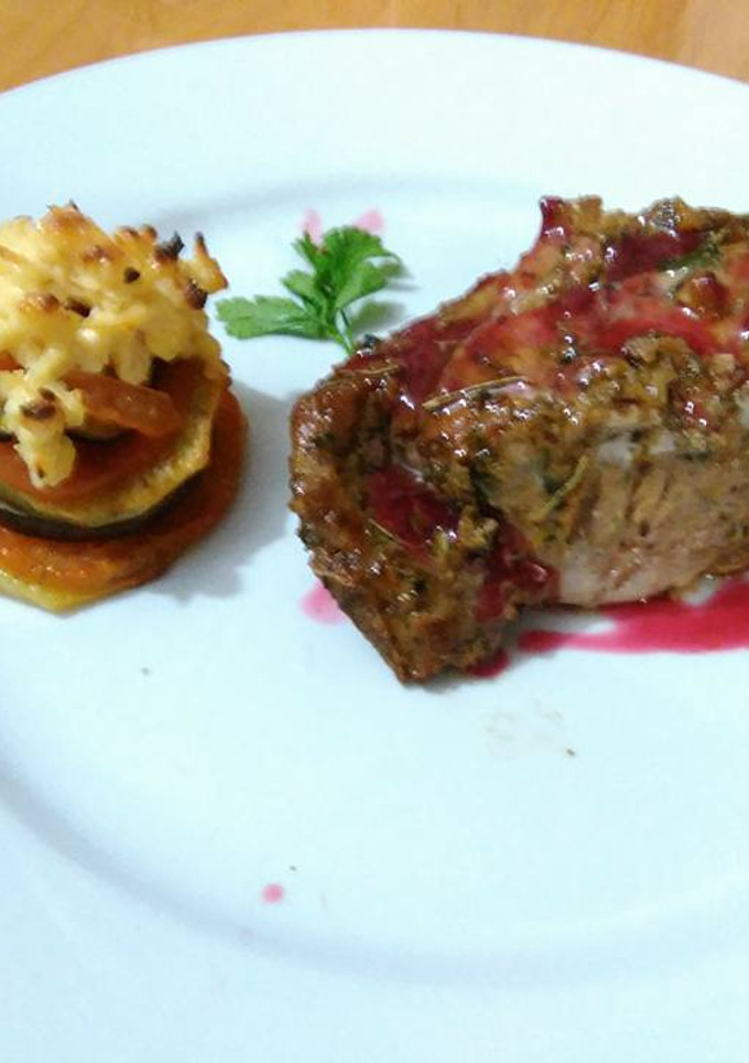 Una foto de Carre de cerdo macerado en finas hierbas con salsa de cítricos y frutos rojos, con torre de vegetales gratinado