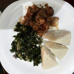 A picture of Goat stew served with ugali and spinach.