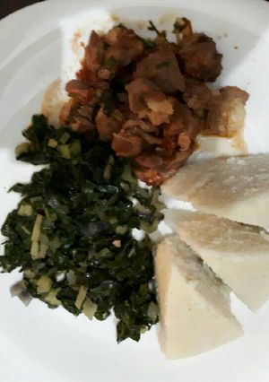 A picture of Goat stew served with ugali and spinach.