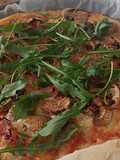 Pizza casera de champiñones, jamón y rúcula