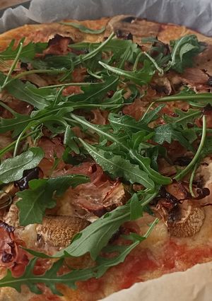 Una foto de Pizza casera de champiñones, jamón y rúcula