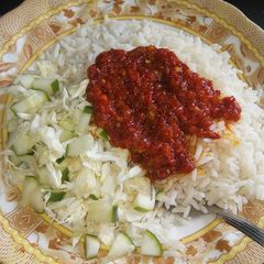 A picture of Rice and stew with cabbage and cucumber.