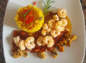 Una foto de Mariscos, con salsa de tomates y arroz con azafrán y alcaparras