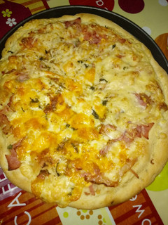 Una foto de Pizza de jamón de york bacon con doble quesos variados con albahaca a la piedra