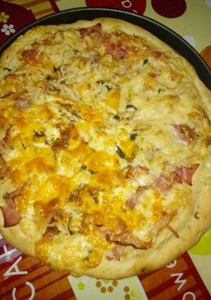 Una foto de Pizza de jamón de york bacon con doble quesos variados con albahaca a la piedra
