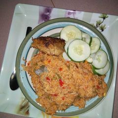 A picture of Jollof rice with chicken and sliced cucumber.