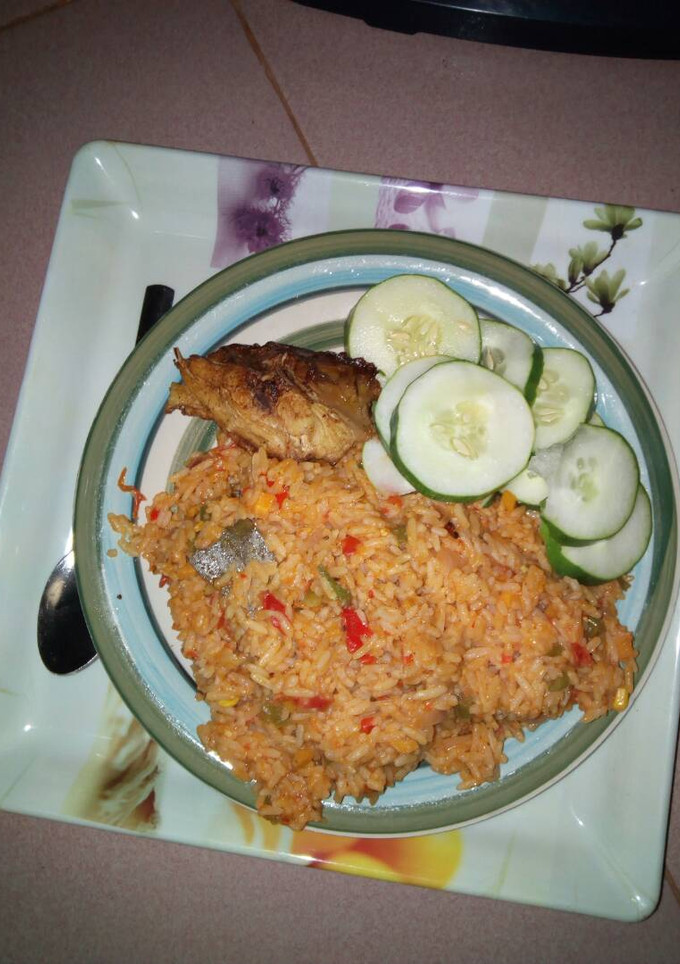 A picture of Jollof rice with chicken and sliced cucumber.