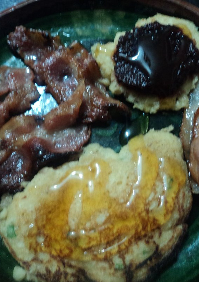 Una foto de Hot cakes navideños con albahaca y amaranto, acompañados de tocino, miel y mermelada de chile correa