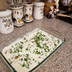 A picture of Slices of chicken with potatoes and white sauce.