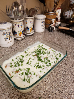A picture of Slices of chicken with potatoes and white sauce.