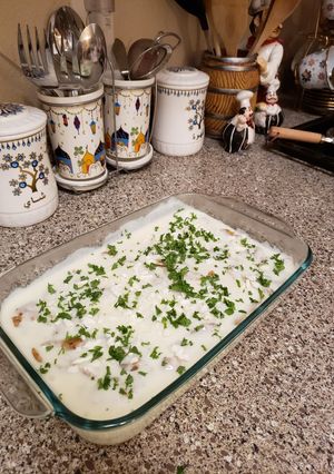 A picture of Slices of chicken with potatoes and white sauce.