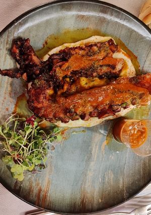 Una foto de Pulpo a la brasa sobre cama de aguacate con salsa picante