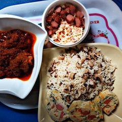 A picture of Rice and beans with stew and coleslaw with boiled egg.