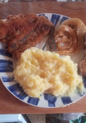 Una foto de Merluza frita con puré aros de cebolla y berenjena