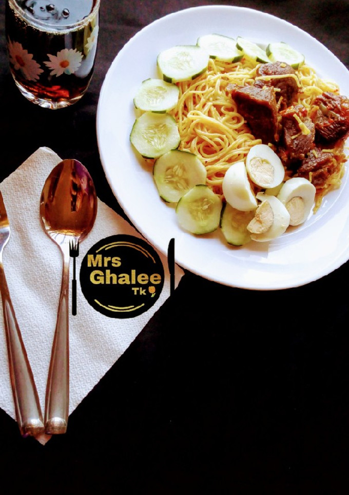A picture of Jollof sphagetti with fried meat and cucumber and eggs and coke.